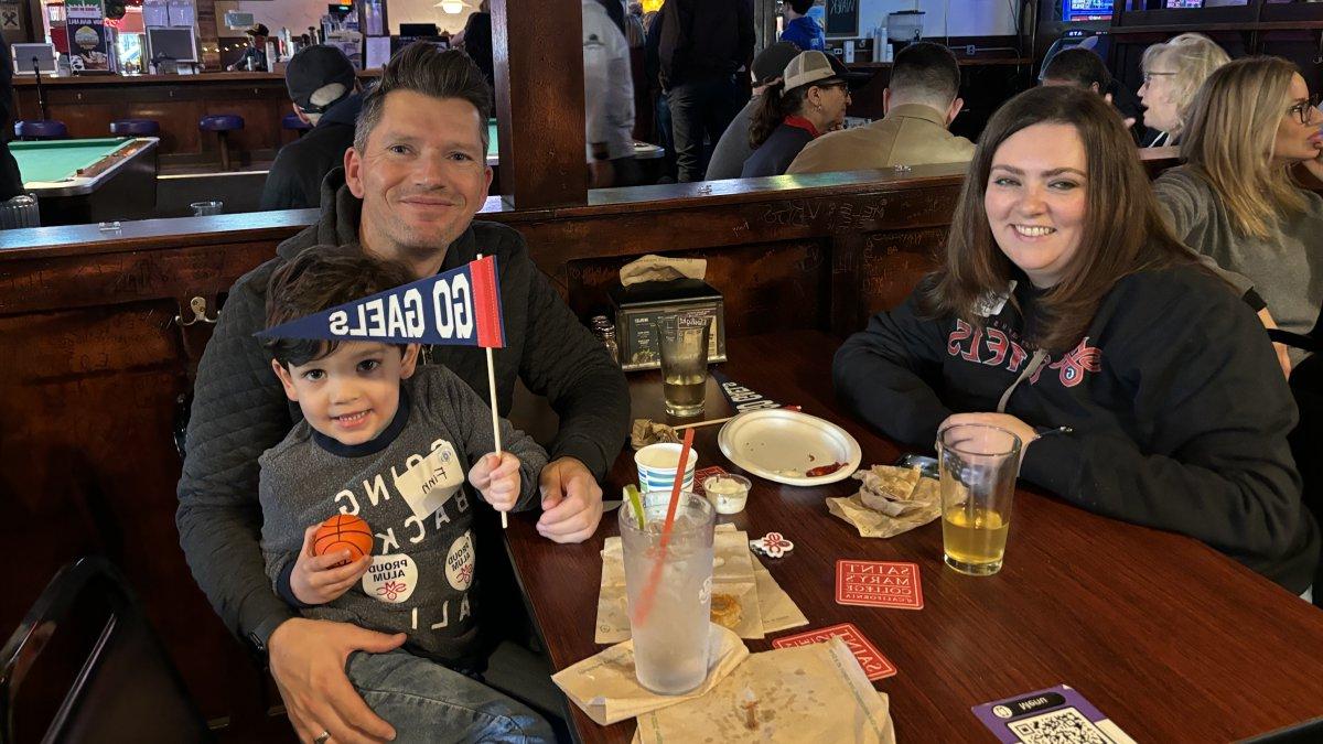 A man, woman, and young child holding Saint Mary's apparel and pennants sit at a restaurant booth.